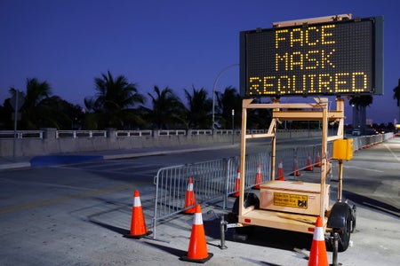 An illuminated sign by a roadway says "Face Masks Required."