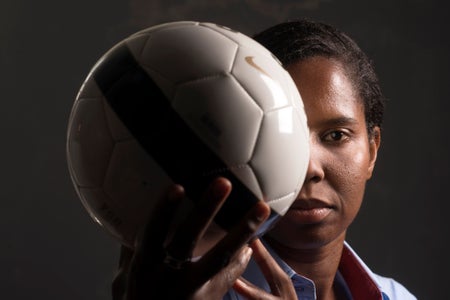 Briana Scurry holding a white soccer ball which partly obscures her face
