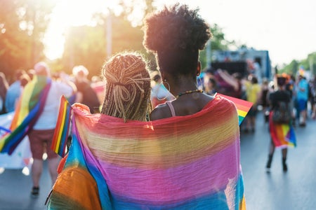 Rear view of young female couple walking, draped in pride flag