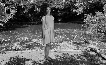 Maria Konnikova waring a white dress standing in front of a pond (black and white image).