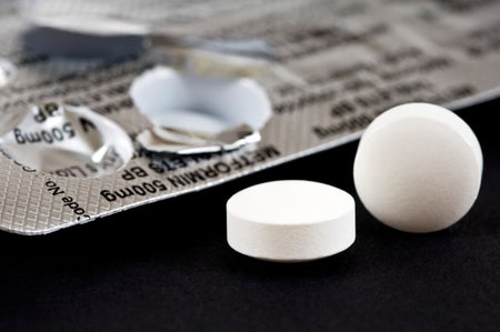 Horizontal macro close up of a blister pack of pills and two Metformin tablets on a black background