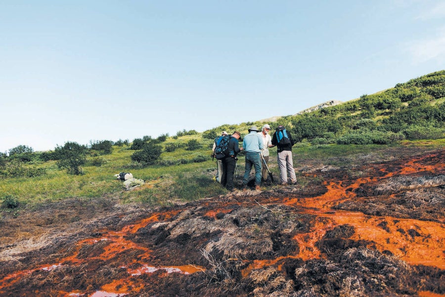 Four men huddle together near rust stained water.