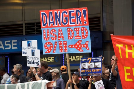 Protesters hold up signs, including a large one that says "Danger! USA Did 9/11."