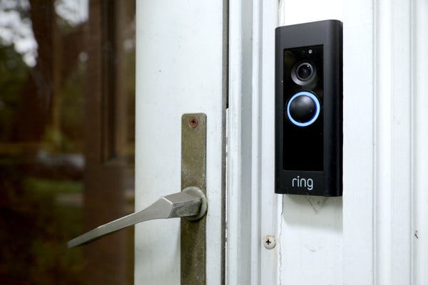 A doorbell device with a built-in camera mounted on a white door with shabby handle.