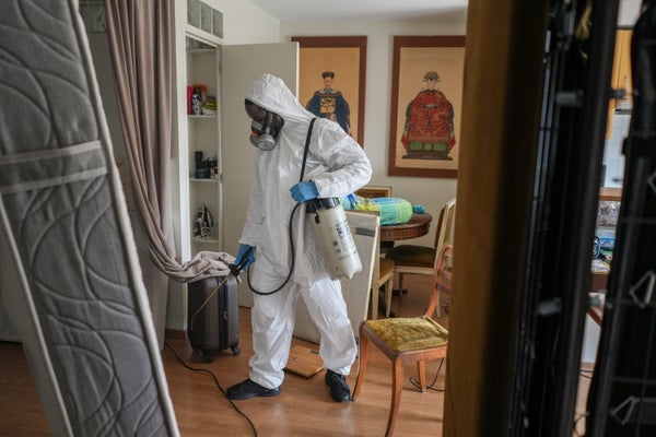 A pest control worker wearing a full body hazmat suit spraying pesticides inside an apartment