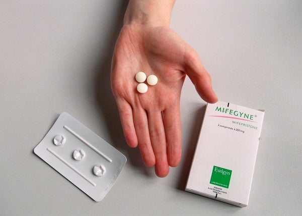 Mifepristone pills held in an open palm alongside the medication box