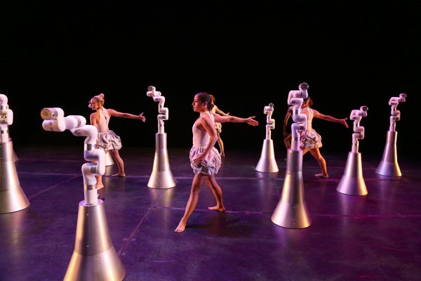 Robots interact with live dancers in a stage performance.