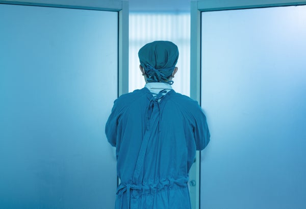 A doctor in scrubs shown from behind in front of double doors