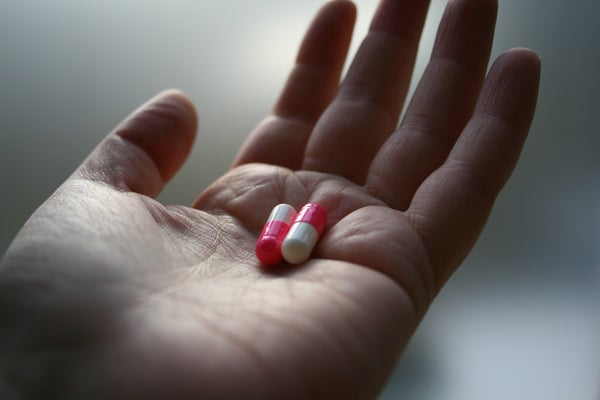 A hand holding two red/white pills