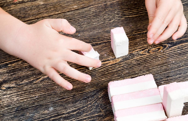 A kid's hands playing with sticky pink and white striped marshmallows