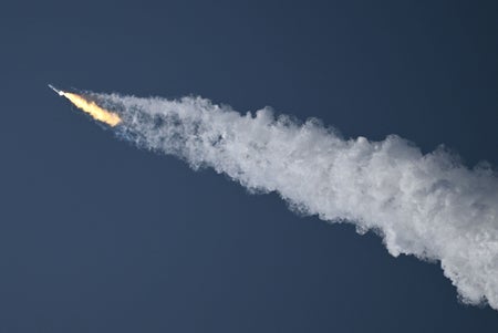 Rocket in blue sky trailed by exhaust plume