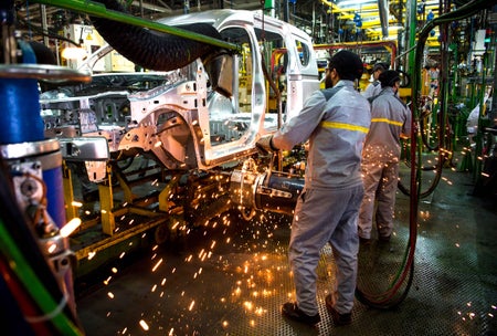 Factory employees in jumpsuits work on a car assembly line at the Renault-Nissan Tanger with sparks flying.