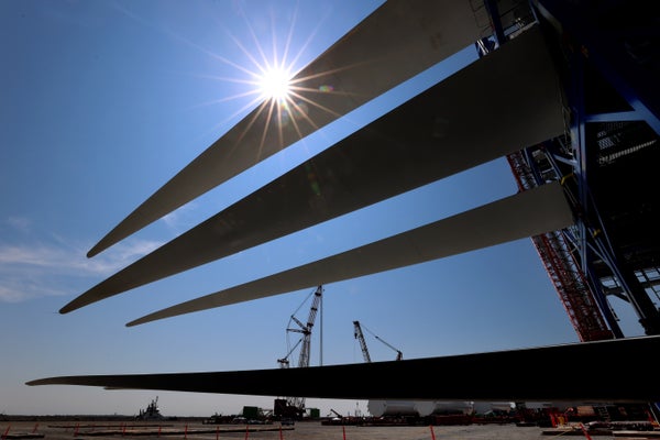 The sun shining through 3 stacked turbine blades with crane background