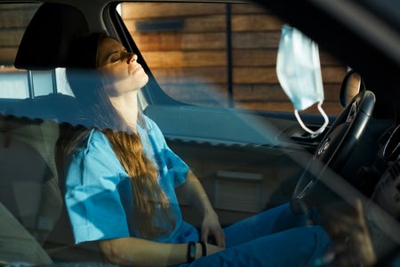 A female nurse is resting inside her car.