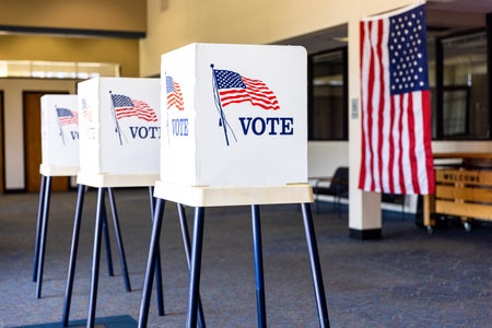 Three voting booths lined up with an American flag in the background.