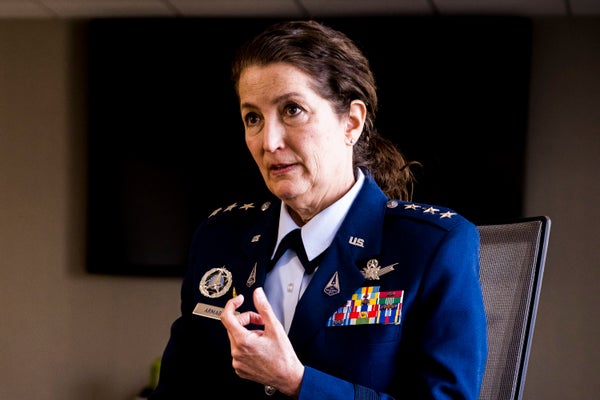 A woman in a dark blue military leadership uniform is centered in the frame