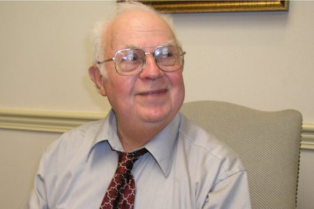 Portrait of Donald Triplett in grey shirt and red tie and glasses.
