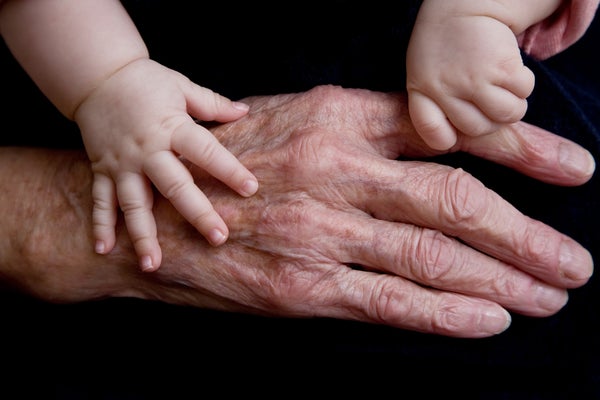 Elderly hand with baby hands shown on black backdrop.