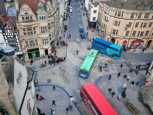Oxford City intersection from above showing pedestrians, bikes and three colorful buses.