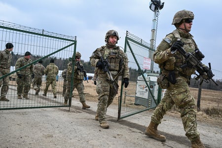 American soldiers walk through a fenced area.