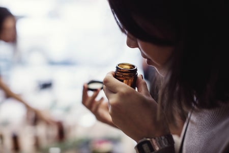 A woman smelling a jar close to her nose.