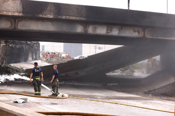 Two firemen stand near a collapsed portion of an interstate bridge.