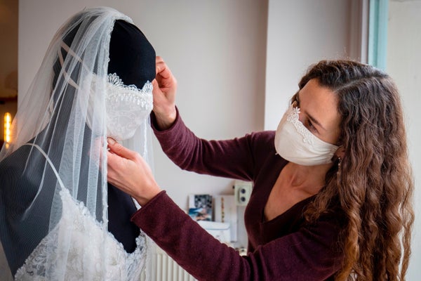 A woman wearing a mask works on a black mannequin wearing a veil.