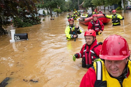 Rescuers wade through deeply flooded neighborhood, suited in bright red gear.