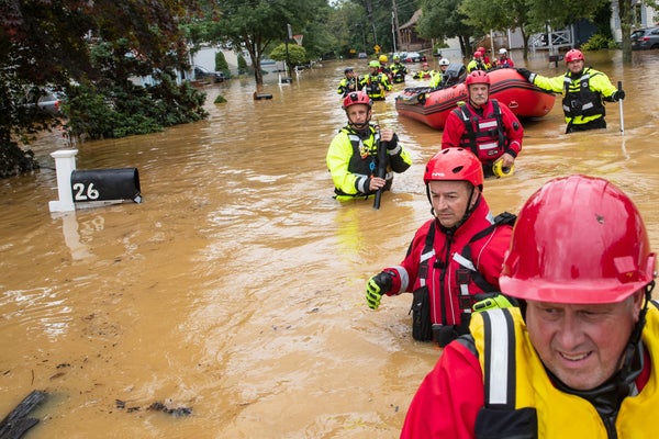 Rescuers wade through deeply flooded neighborhood, suited in bright red gear.