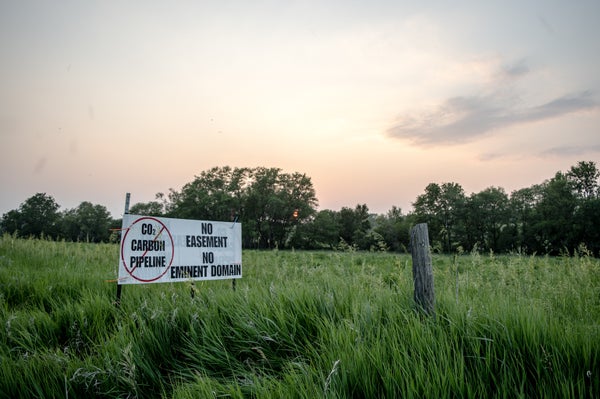 A sign in a field of long grass that with the words "CO2 Carbon Pipeline" crossed out on the left. On the righthand side reads, "No Easement No Eminent Domain"