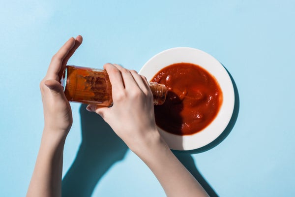 Cropped view of woman pouring ketchup from bottle to plate.