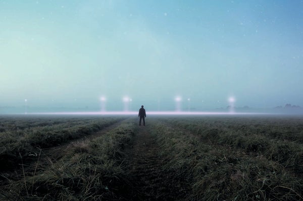 A person standing in an open field at dusk, with lights in the sky.