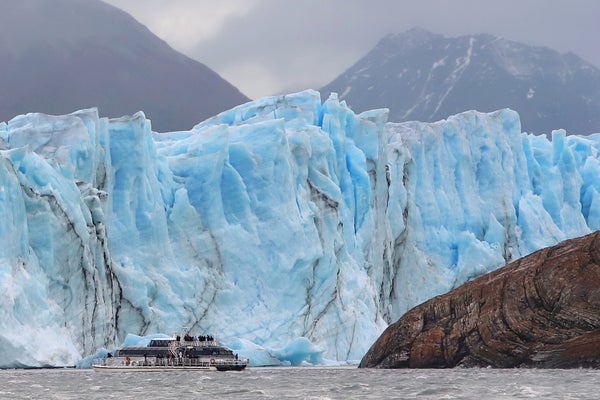 A boat travels in front of a large blue glacier.