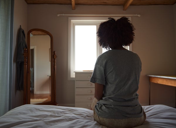 A Black woman is sitting on a bed, shown from behind.