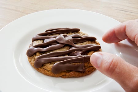 A cookie atop a plate with a chocolate swirl on top.