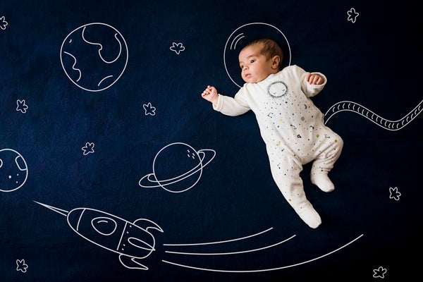 Infant shown on a blue backdrop with white drawings of earth, a space ship, planets and a space helmet on infant's head.