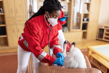 A female health care worker examines a senior woman at home.