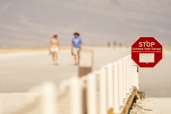 Two people walk in the distance, with an "Extreme Heat Danger" sign seen in the foreground in Death Valley, California.