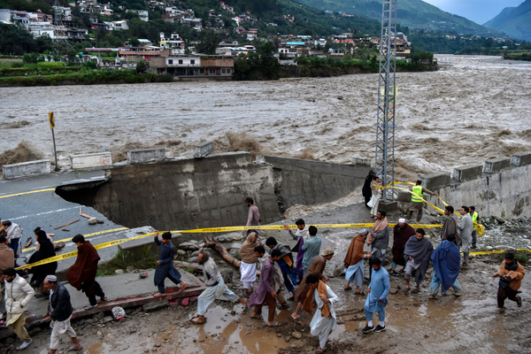 People gather in front of a road damaged by flood waters in Pakistan.