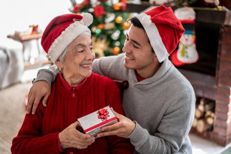 Grandson surprising his grandmother both wearing Santa hats in front of Christmas tree