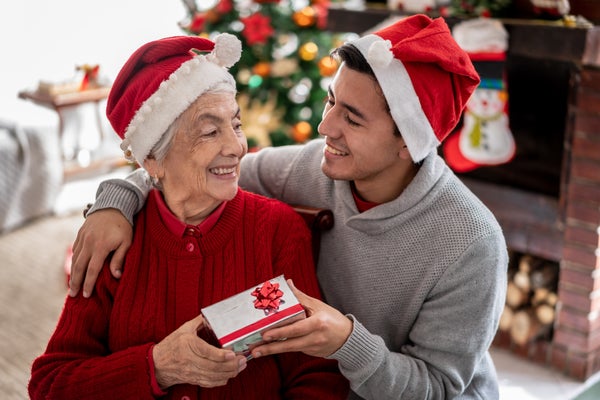 Grandson surprising his grandmother both wearing Santa hats in front of Christmas tree