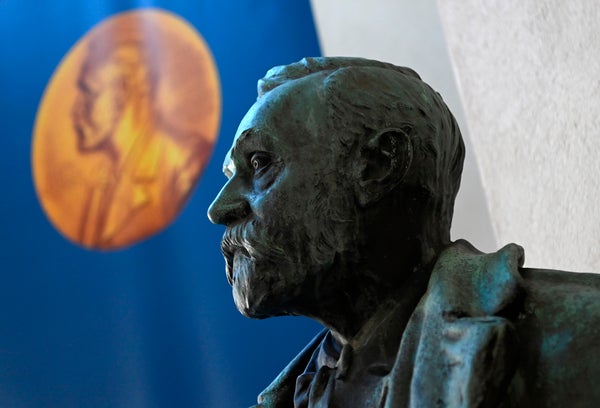 A bust of Alfred Nobel with the gold Medal displayed on the blue background wall