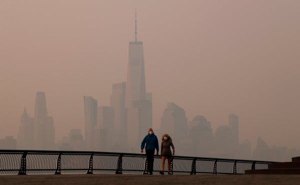 Two people wearing masks walk along the Hudson River promenade with Manhattan Skyline