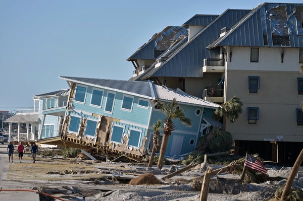 Three people walk along a street in Mexico Beach, Fla., past several homes that were damaged and pushed off their foundation