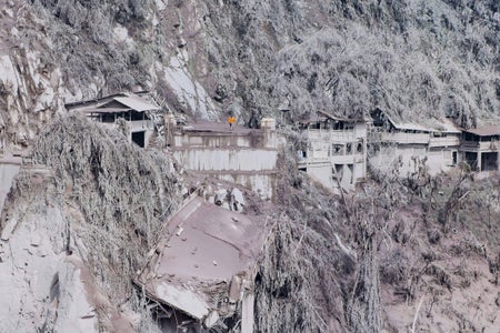 A person walks among ash-covered rubble.