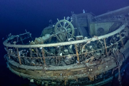 Underwater shipwreck showing ship's wheel and deck.