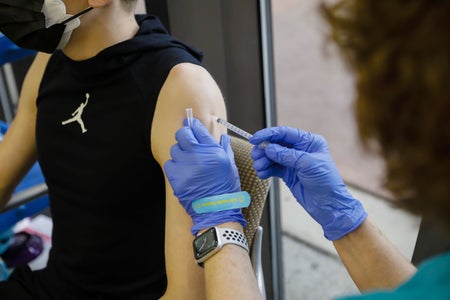 Healthcare worker giving vaccine to teenager in sleeveless t-shirt.