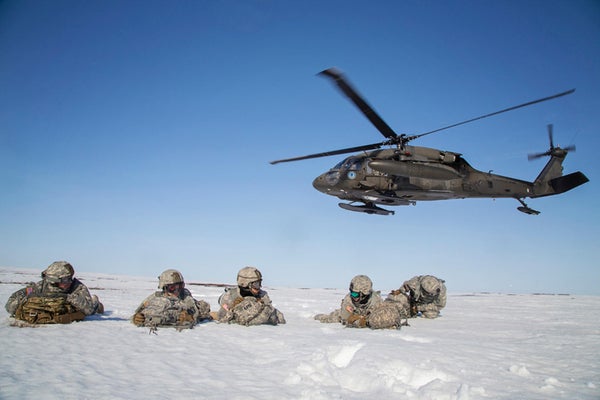 Paratroopers in snow below helicopter.