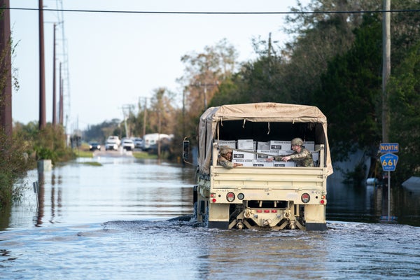 National Guardsmen transport meals ready-to-eat in a military vehicle driving through high water.