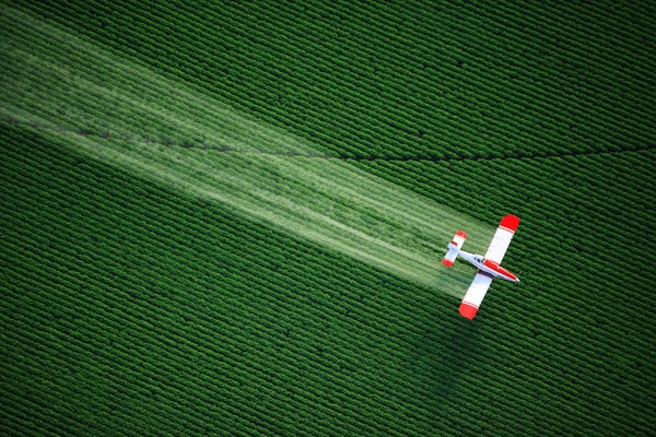 Aerial view of a crop duster flying low, and spraying agricultural chemicals, over lush green fields